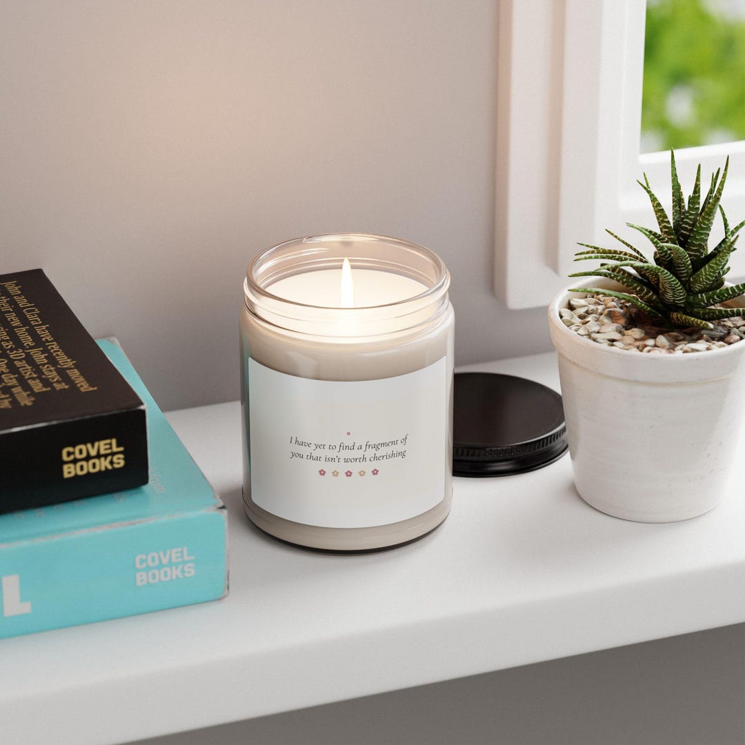 A 9 oz soy candle in a glass jar, its label printed with a poem line